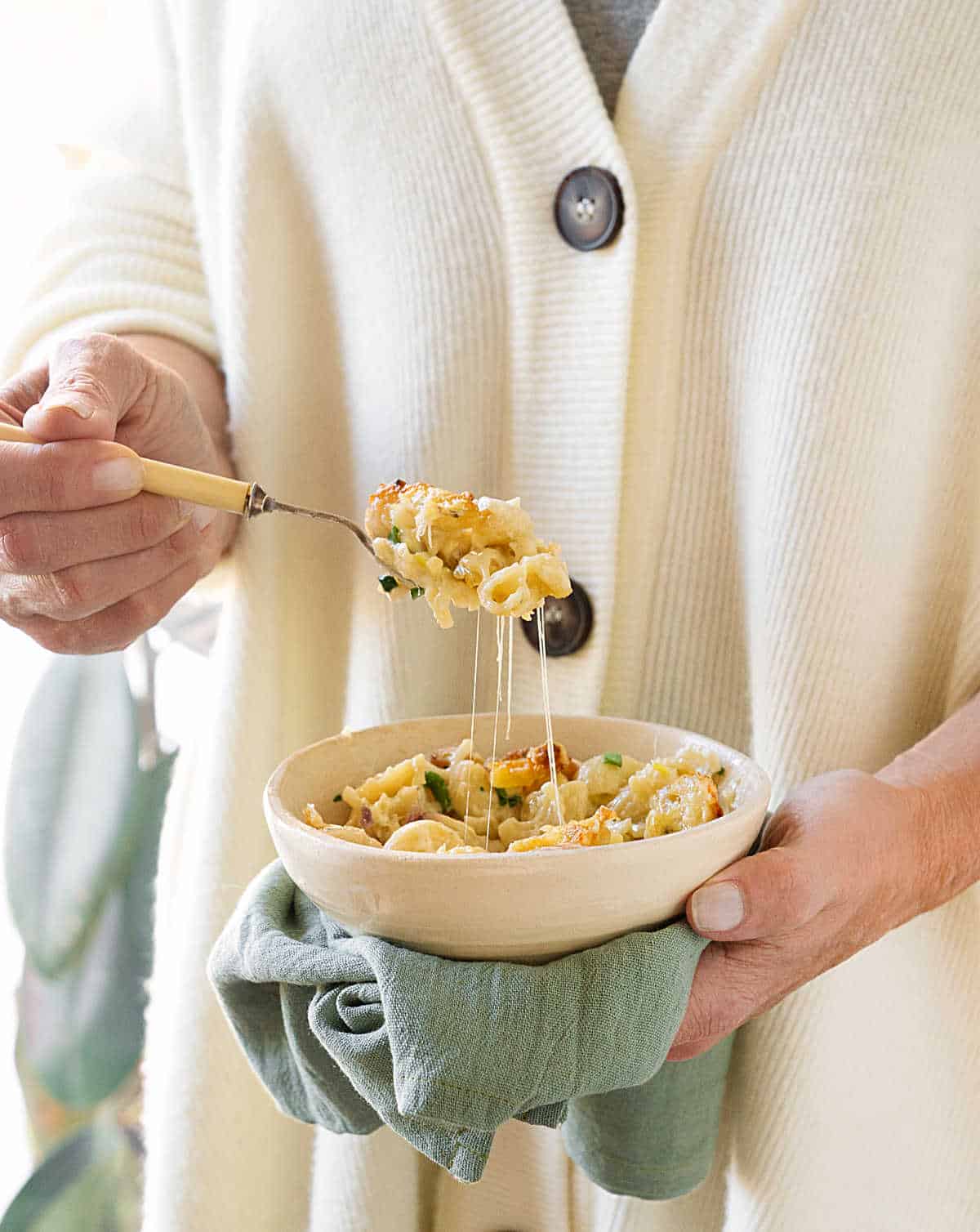 Person in white sweater lifting mac and cheese from a white bowl. 