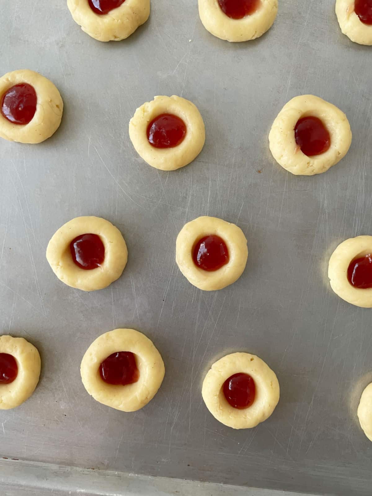 Top view of several jam filled unbaked thumbprint cookies on a metal cookie sheet.