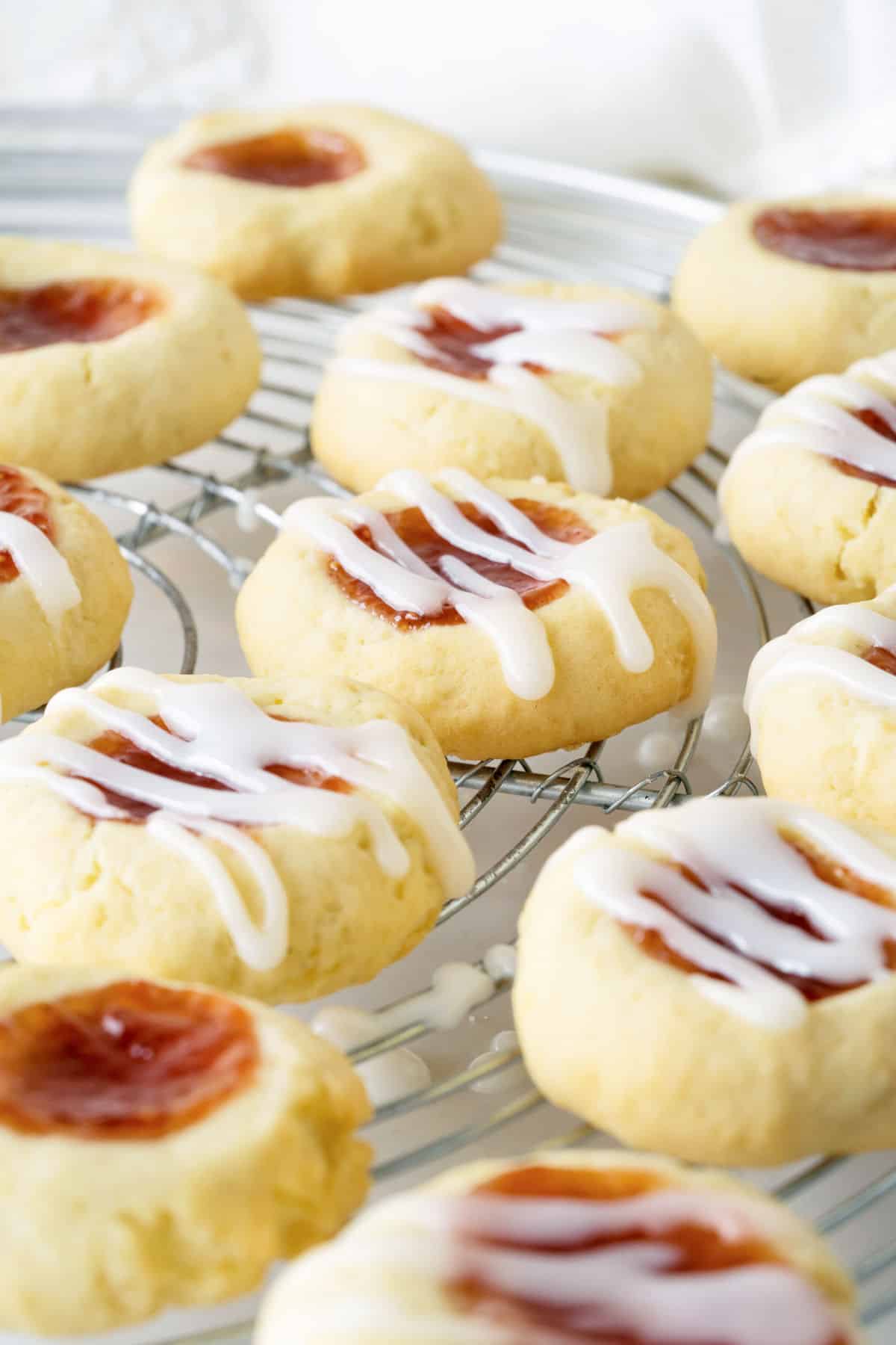 Several jam thumbprint cookies on a wire rack with and without glaze. 