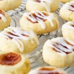 Close up of glazed strawberry jam thumbprint cookies on a wire rack.