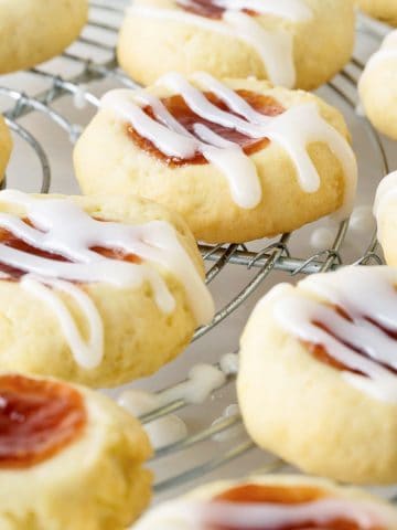 Close up of glazed strawberry jam thumbprint cookies on a wire rack.