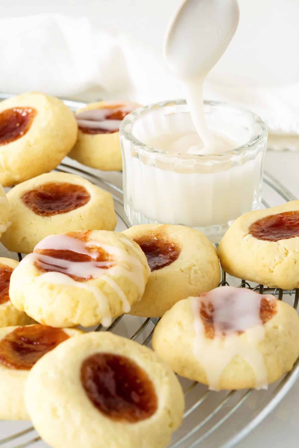 Piled strawberry jam thumbprints on a wire rack with bowl containing glaze.