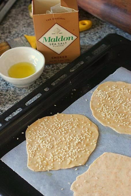 Ottolenghi's Olive Oil Crackers on pan, ready to be baked. Salt and bowl with olive oil