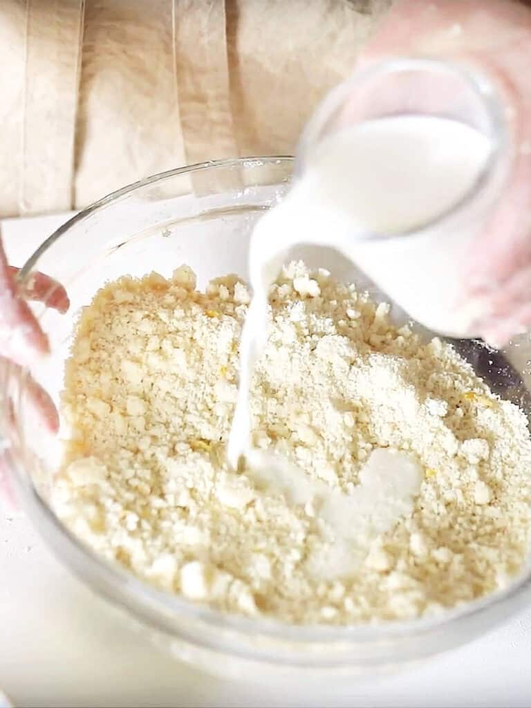 Pouring milk to a scone mixture in a glass bowl. 