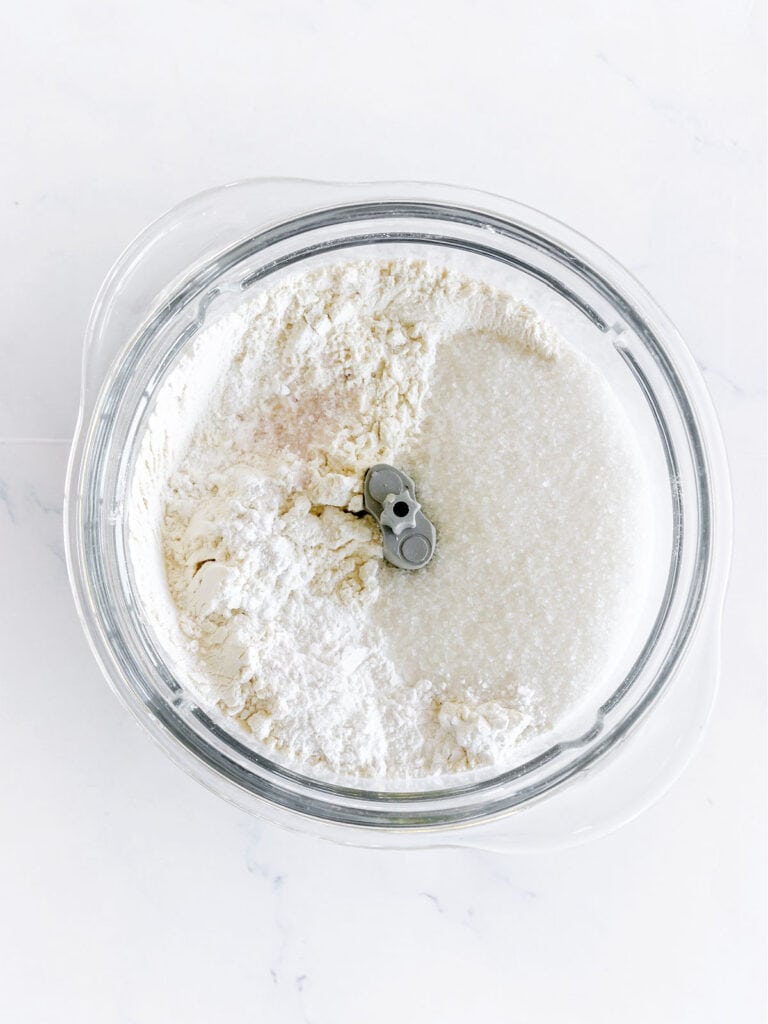 Food processor bowl with dry ingredients for scones. White surface. Top view. 