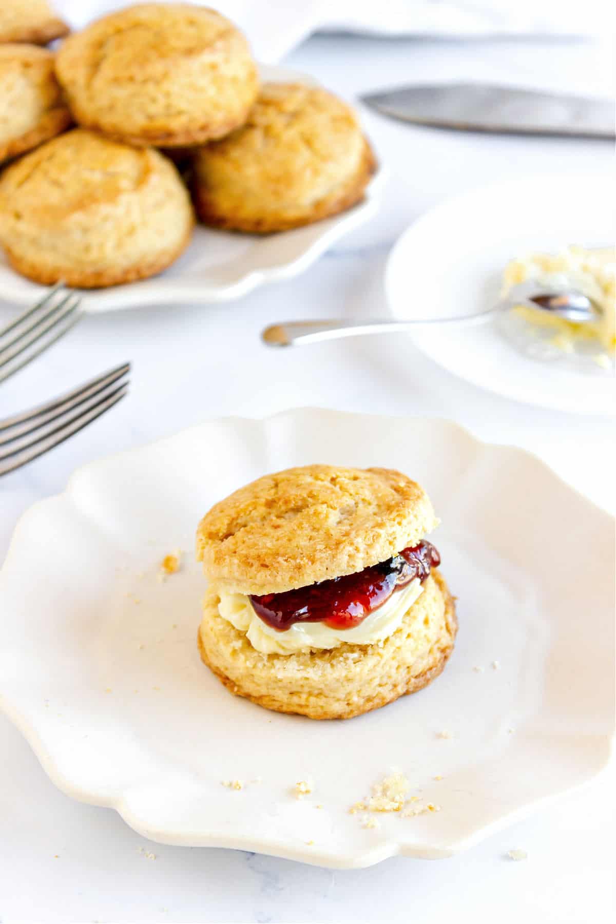 Butter and jam filled scone on a plate. White background with more scones and cutlery.