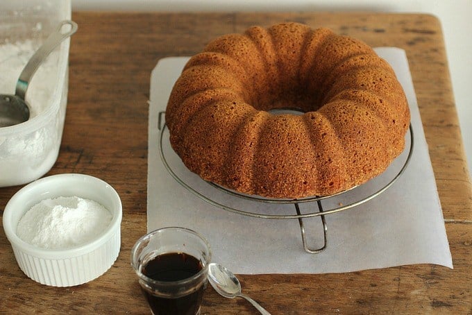 Brown Butter Cake on wire rack, parchment paper on wooden table, powdered sugar, coffee.
