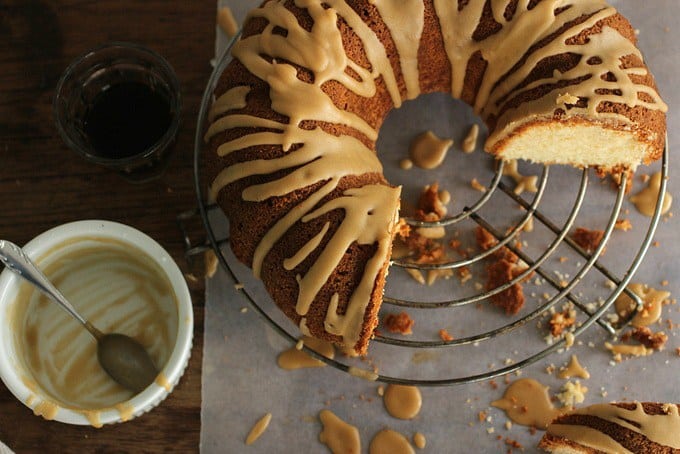 Butter Cake with Coffee Glaze on wire rack, slices missing, white bowl, crumbs on parchment paper
