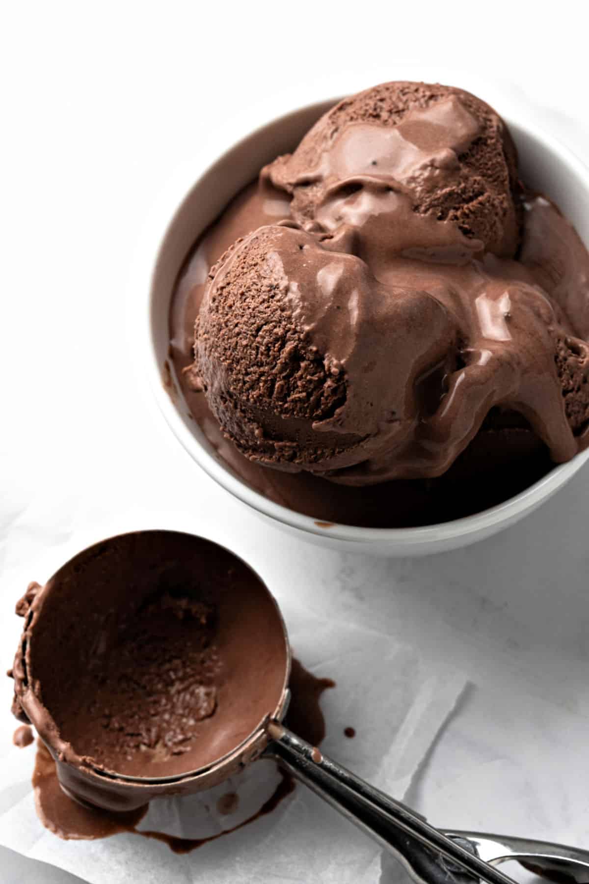 White bowl and metal scoop of Baileys chocolate ice cream. White background. 