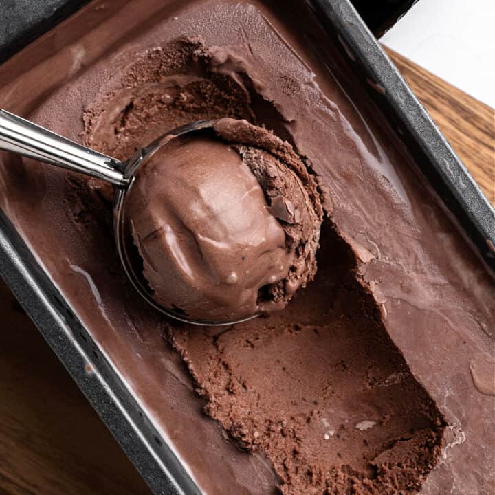 Close up chocolate ice cream in metal loaf with ice cream scoop inside.