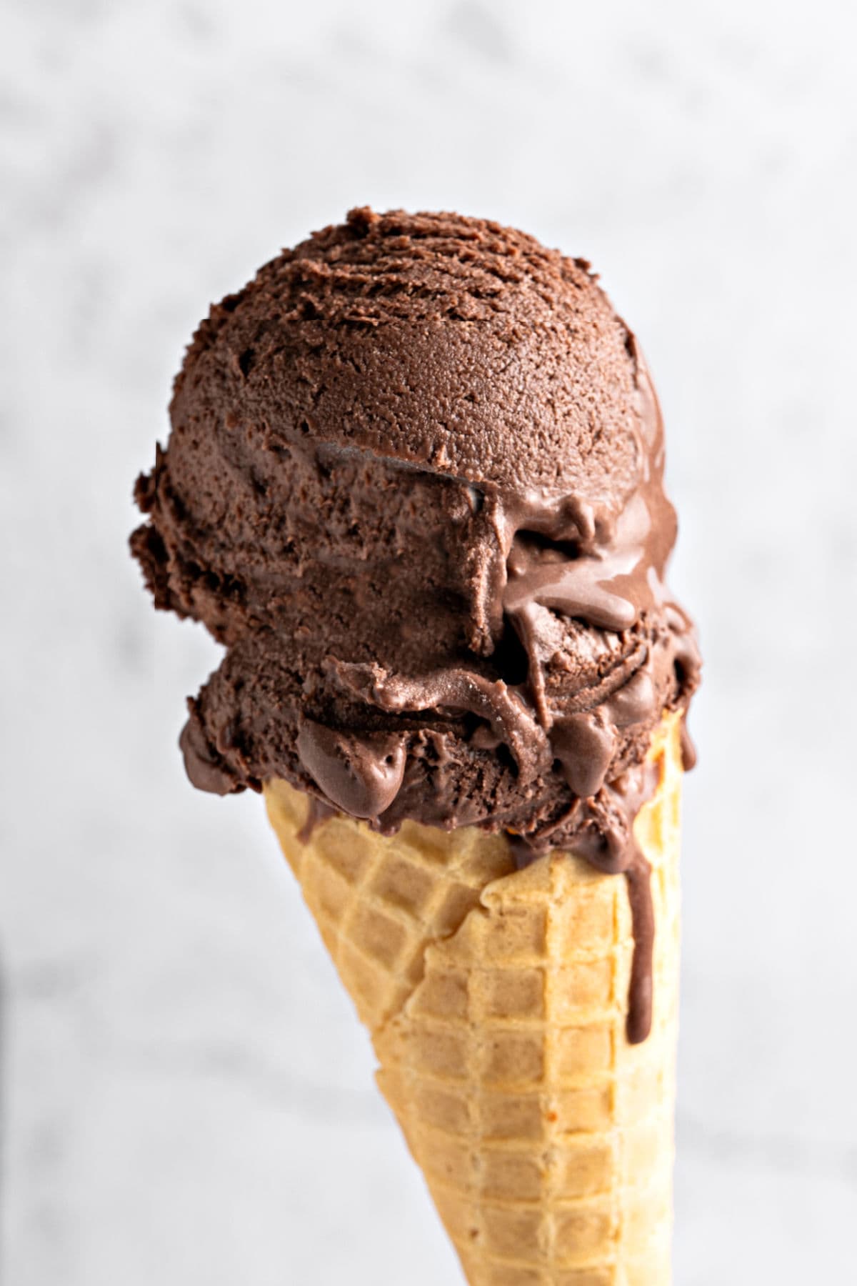 Waffle cone of dark chocolate ice cream. Light gray background.