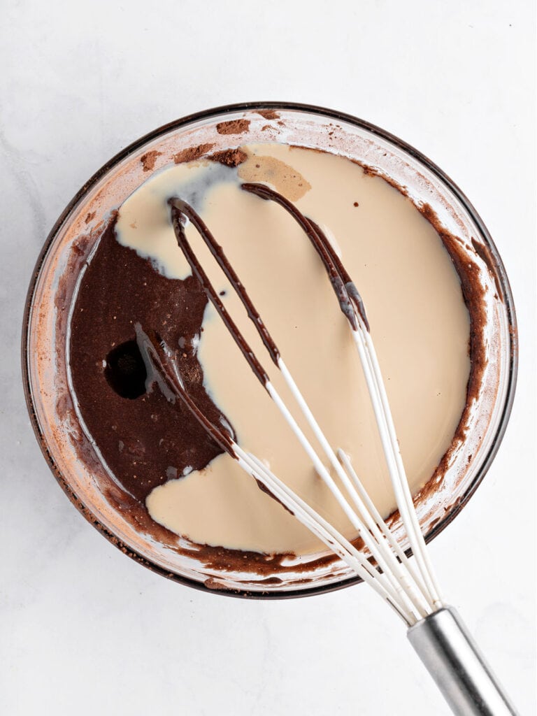 Glass bowl with chocolate mixture and Baileys. White whisk and background. Top view.