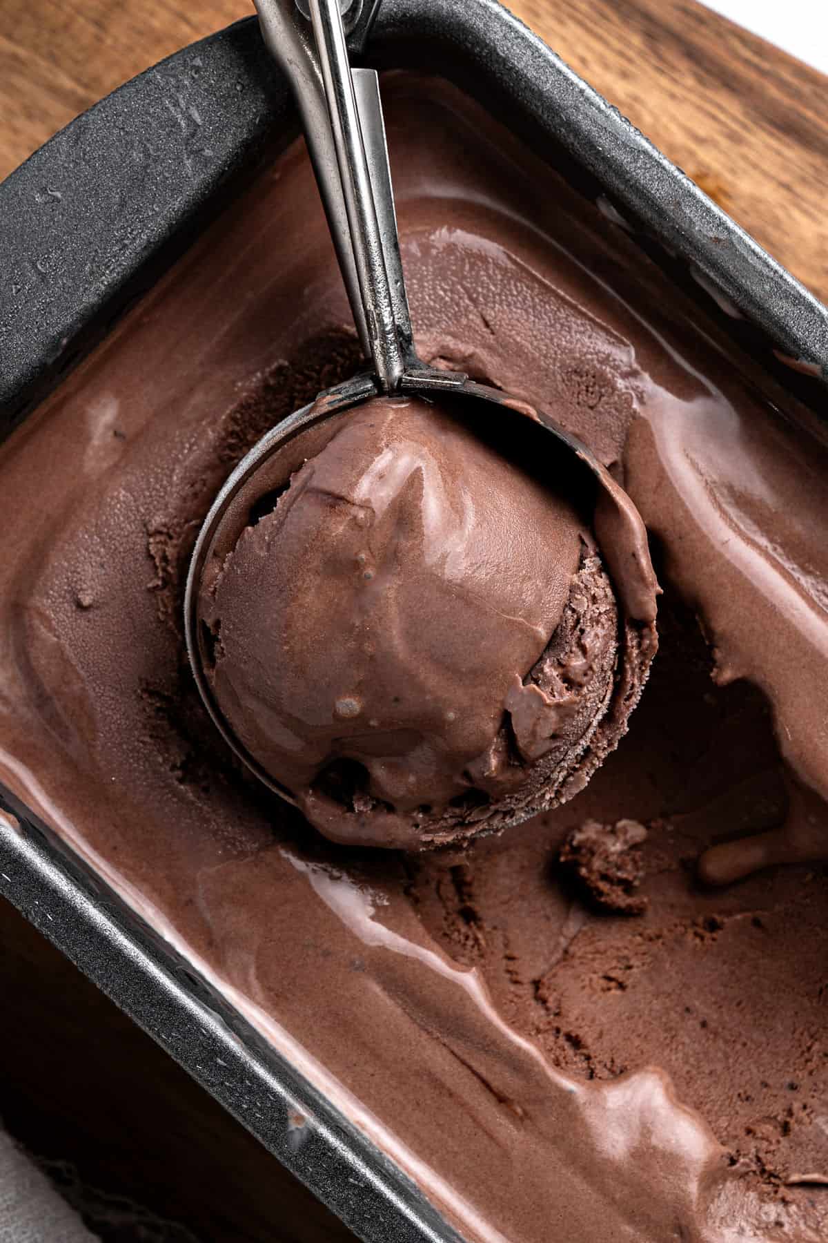 Dark chocolate ice cream in a dark metal loaf with ice cream scoop inside.