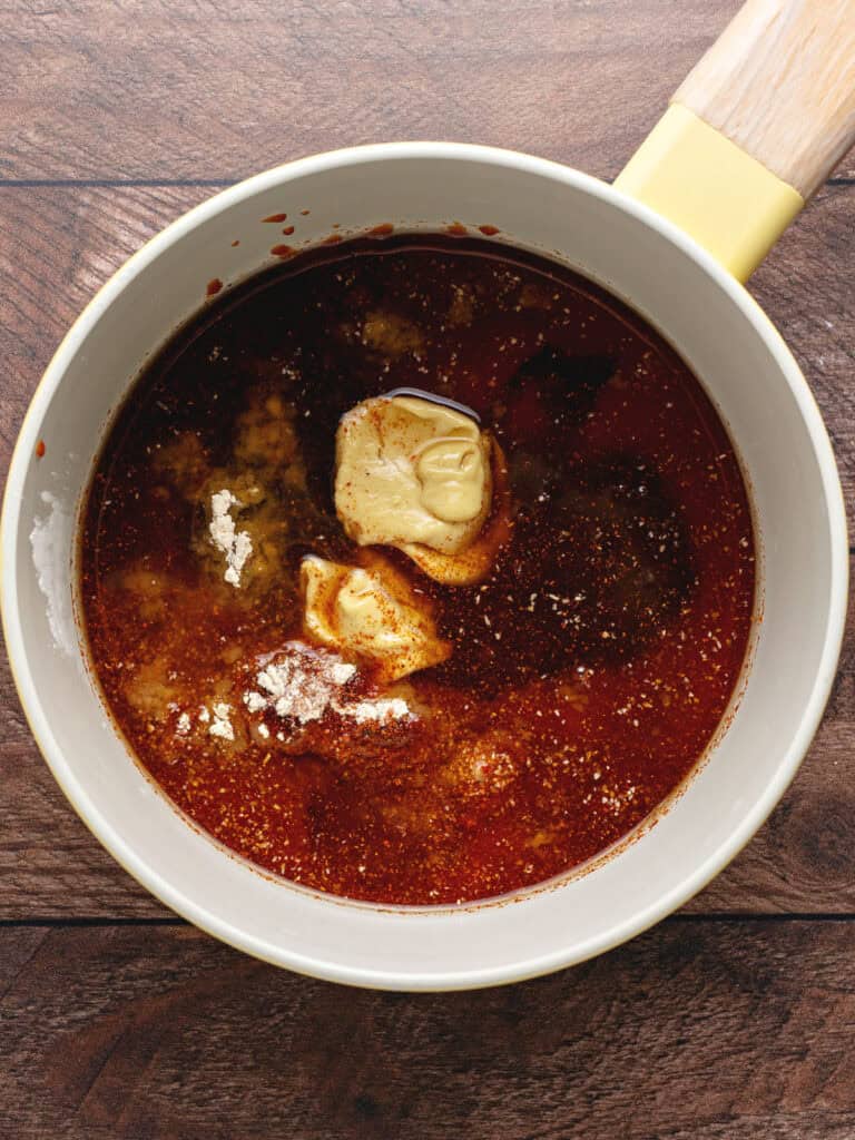 White saucepan with ingredients for barbecue bourbon sauce. Wooden background.