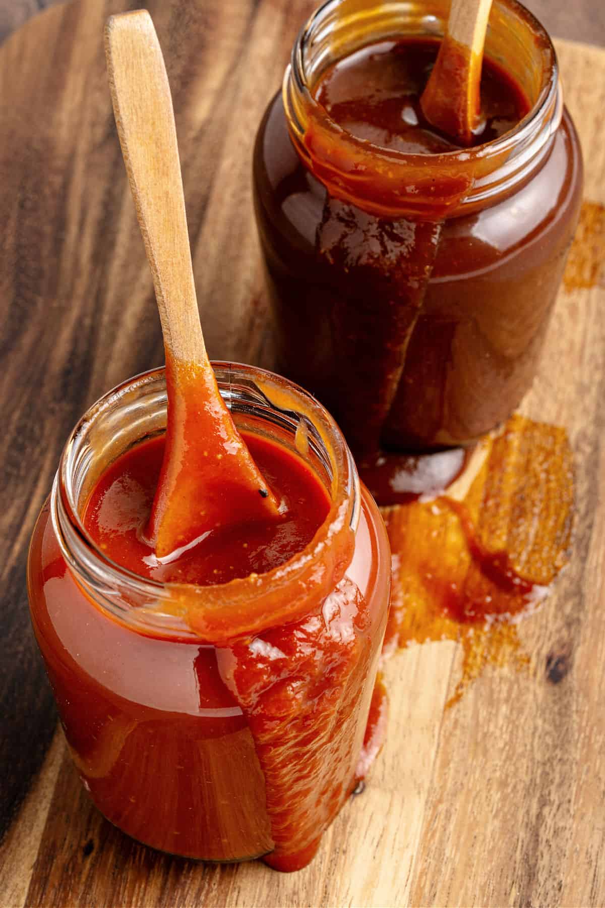 Dripping jars with wooden spoons of bourbon barbecue sauces. Wooden background.