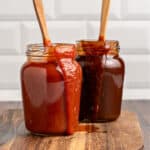 Wooden board with jars of different barbecues sauces. Wooden spoons, subway tile background.