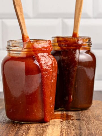 Wooden board with jars of different barbecues sauces. Wooden spoons, subway tile background.