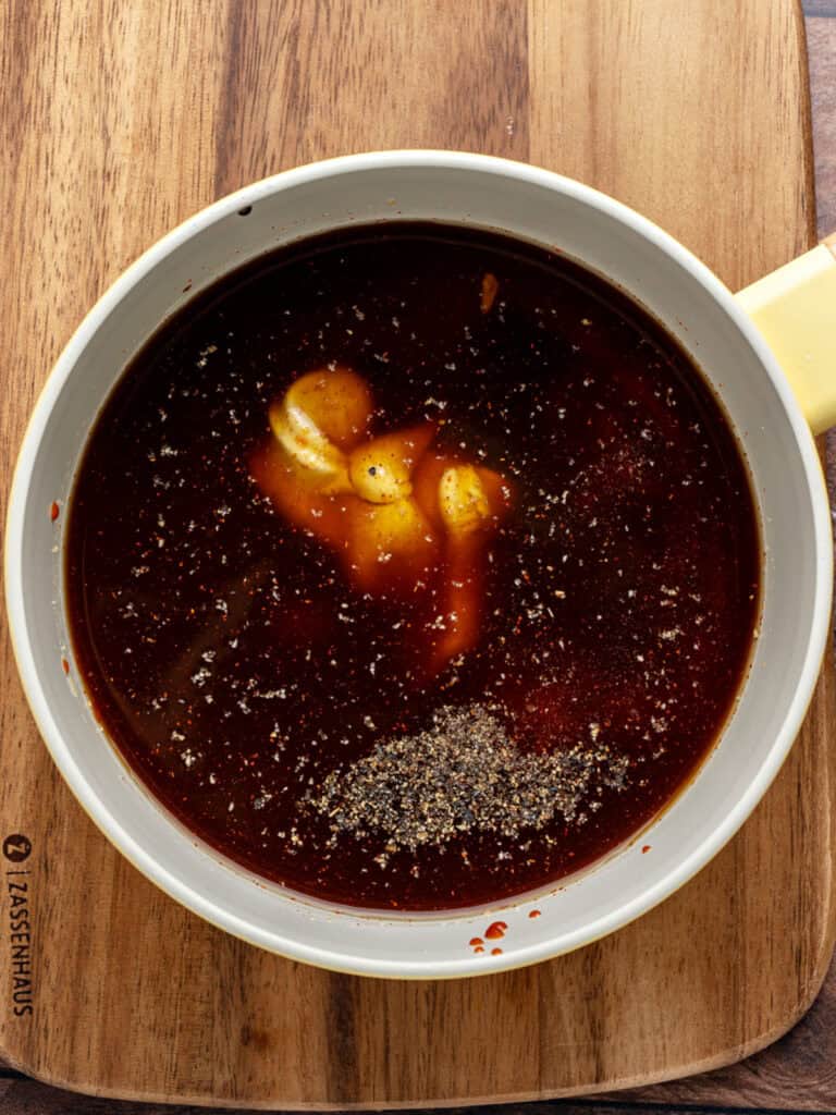 Smoky barbecue bourbon sauce ingredients in a white saucepan. Wooden surface.