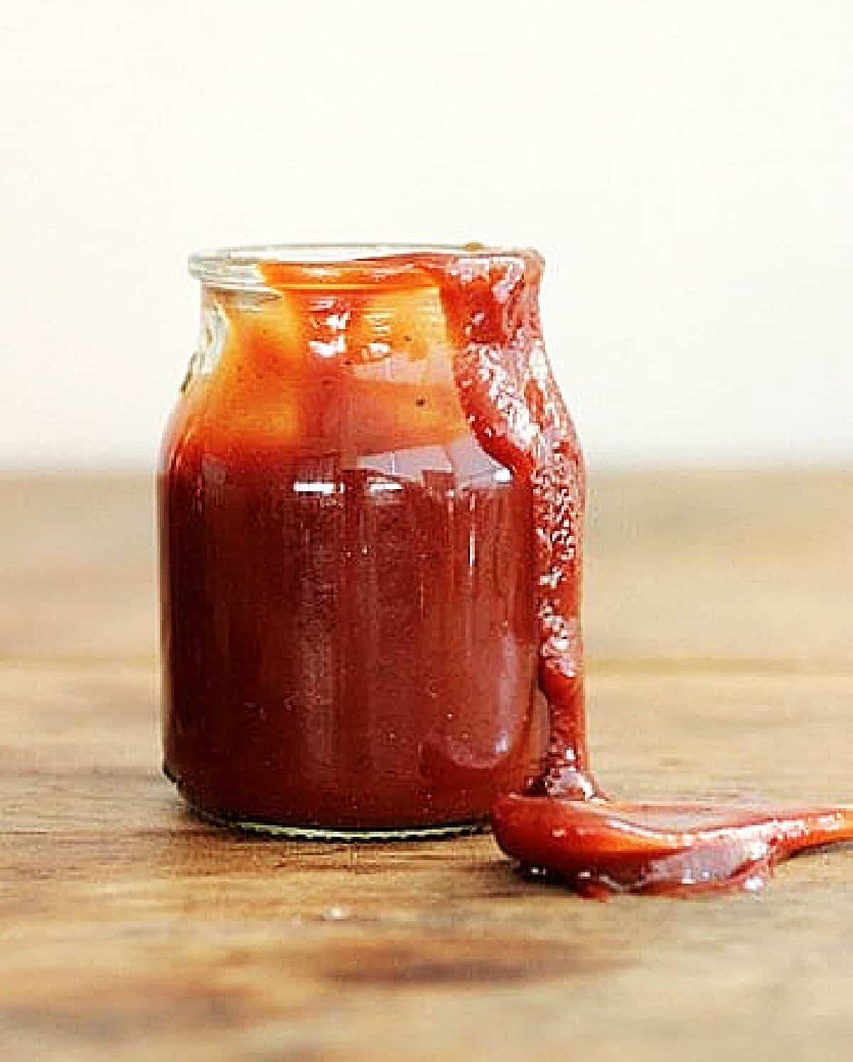 Jar with dripping red barbecue sauce on a wooden surface.