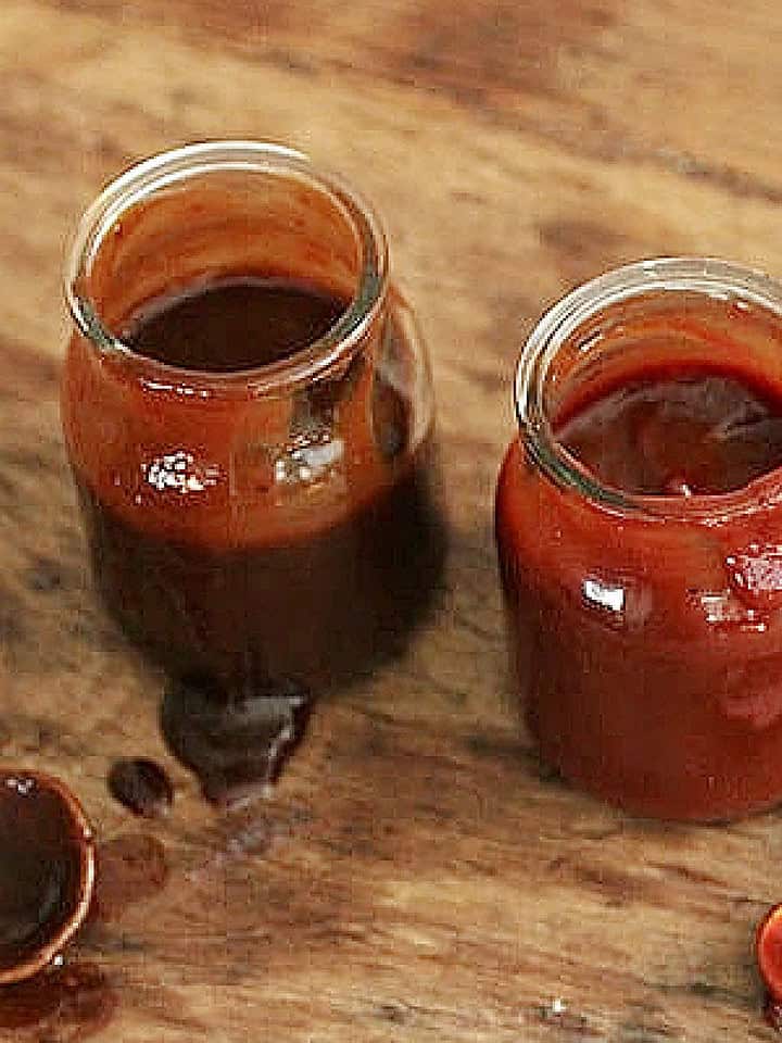 Dripping glass jars of barbecue sauce on a wooden table. Wooden spoons.