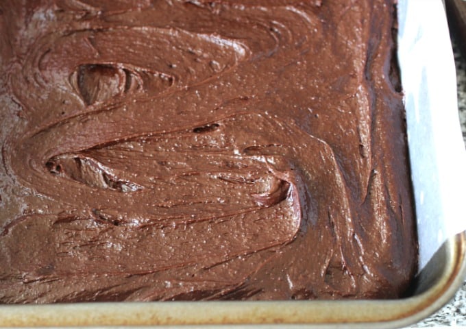 Unbaked brownie batter in metal pan with parchment paper.