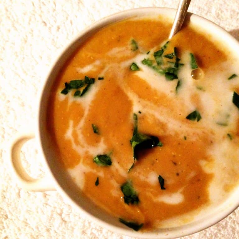 White bowl with orange soup with green specks, white surface