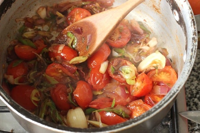 Metal old saucepan with tomatos and onions cooking, a wooden spoon.
