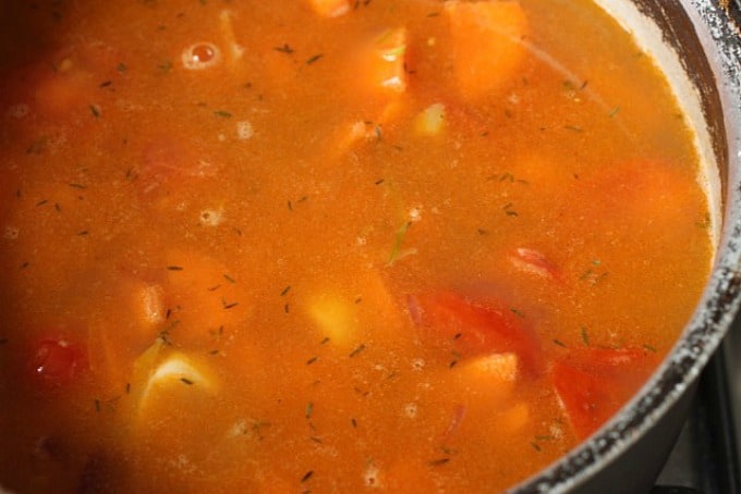Orange colored soup broth in old metal saucepan.