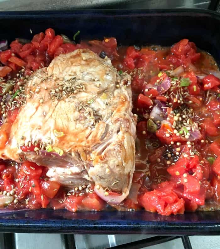 Black oven tray with pork, chopped tomatoes and spices 