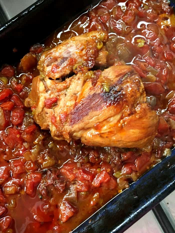 Baked pork shoulder with tomatoes on a black oven pan