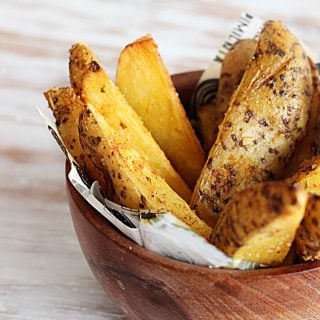 spicy baked potato wedges in wodden bowl on white table