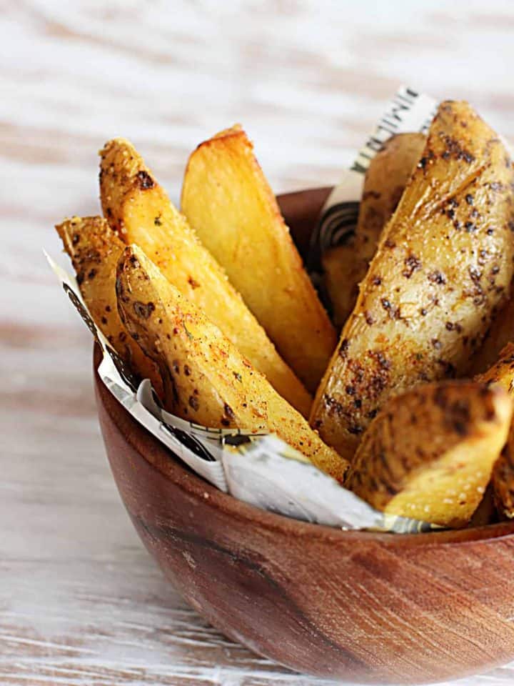 spicy baked potato wedges in wodden bowl on white table