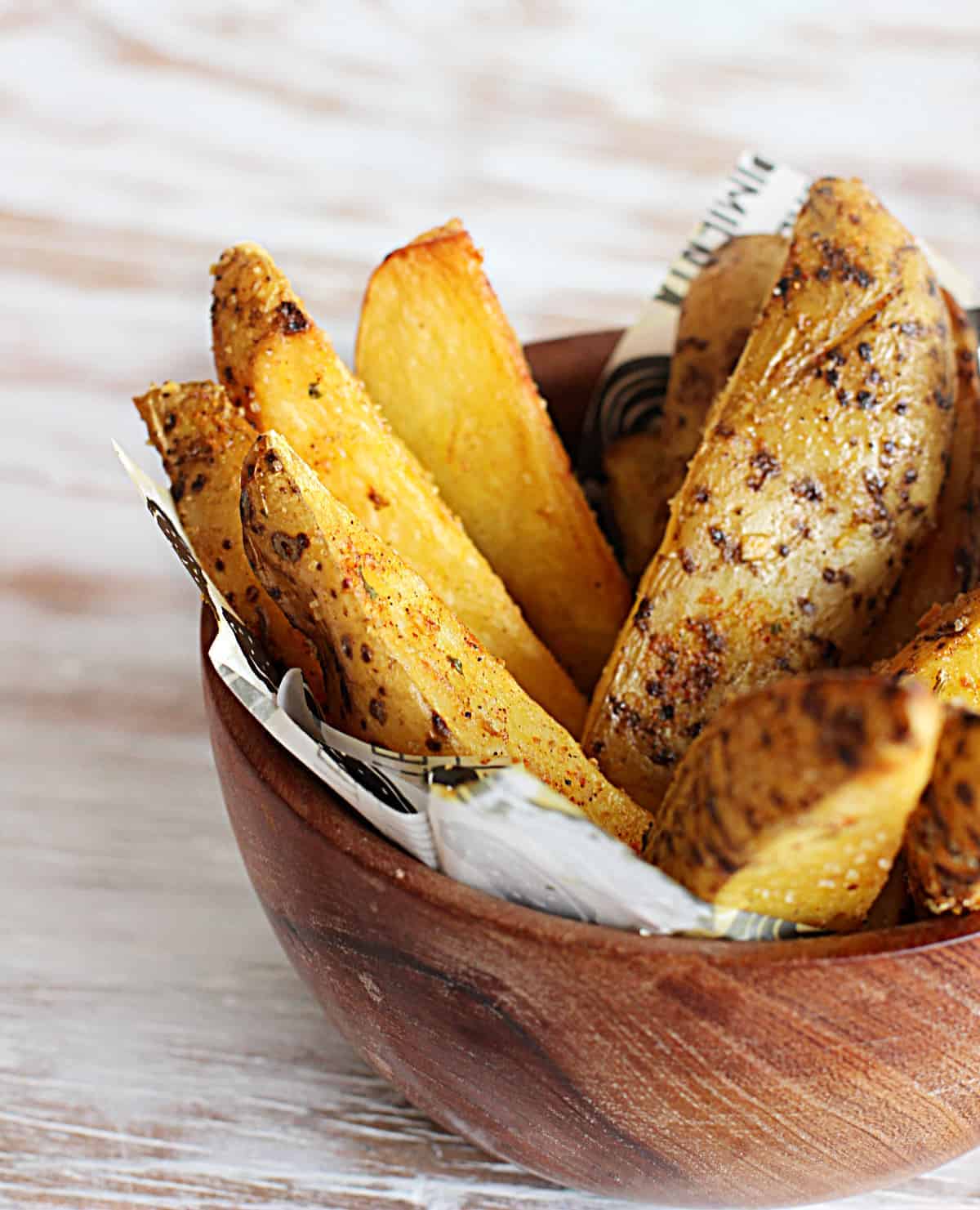 spicy baked potato wedges in wodden bowl on white table