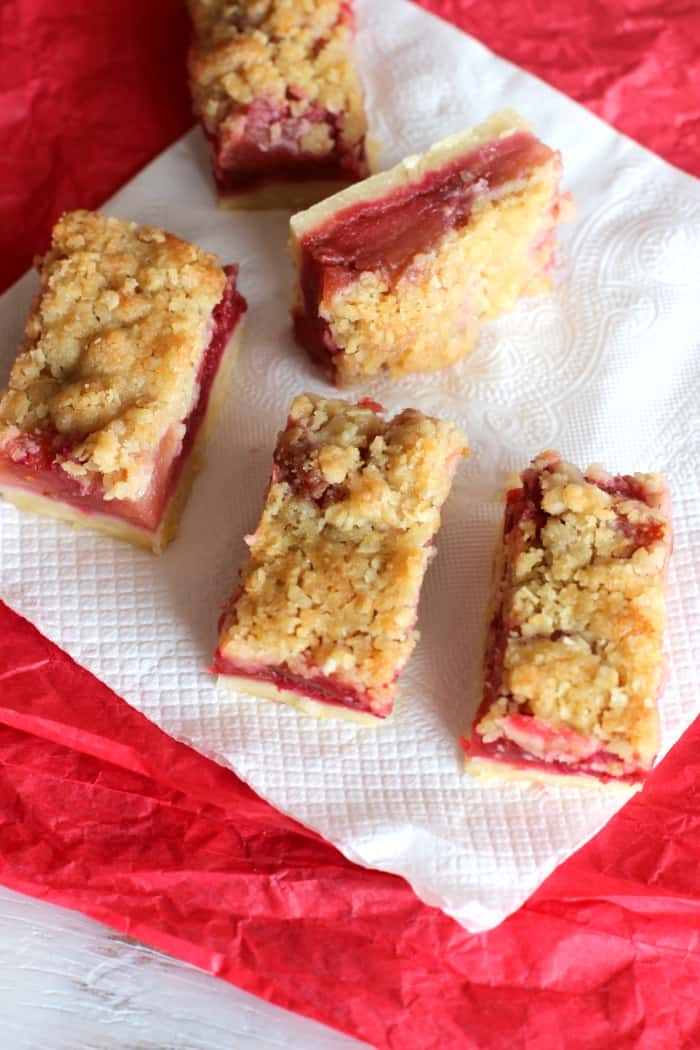 On a red and white surface, squares of apple raspberry crumb bars.