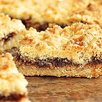 Brown text overlay on squares of jam-filled shortbread bars. Wooden surface.