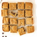 Block of chocolate chip blondies cut into squares on a light beige paper.
