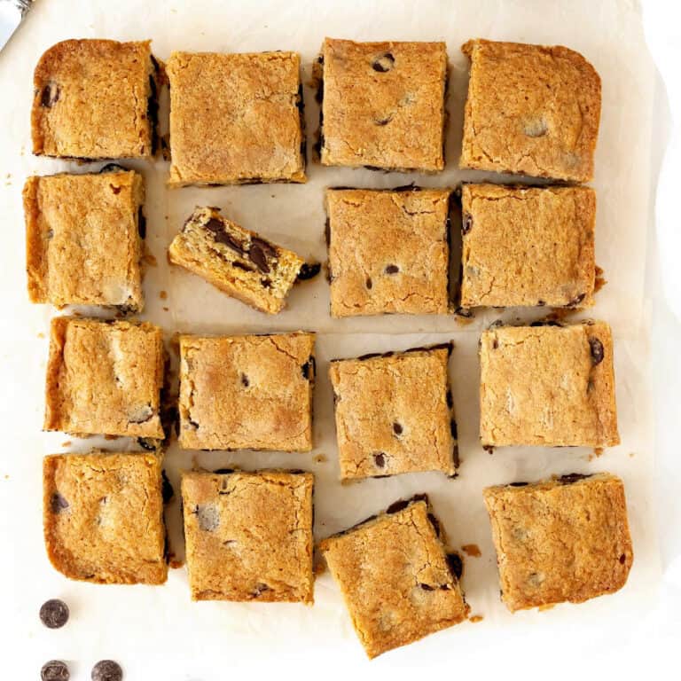 Block of chocolate chip blondies cut into squares on a light beige paper.