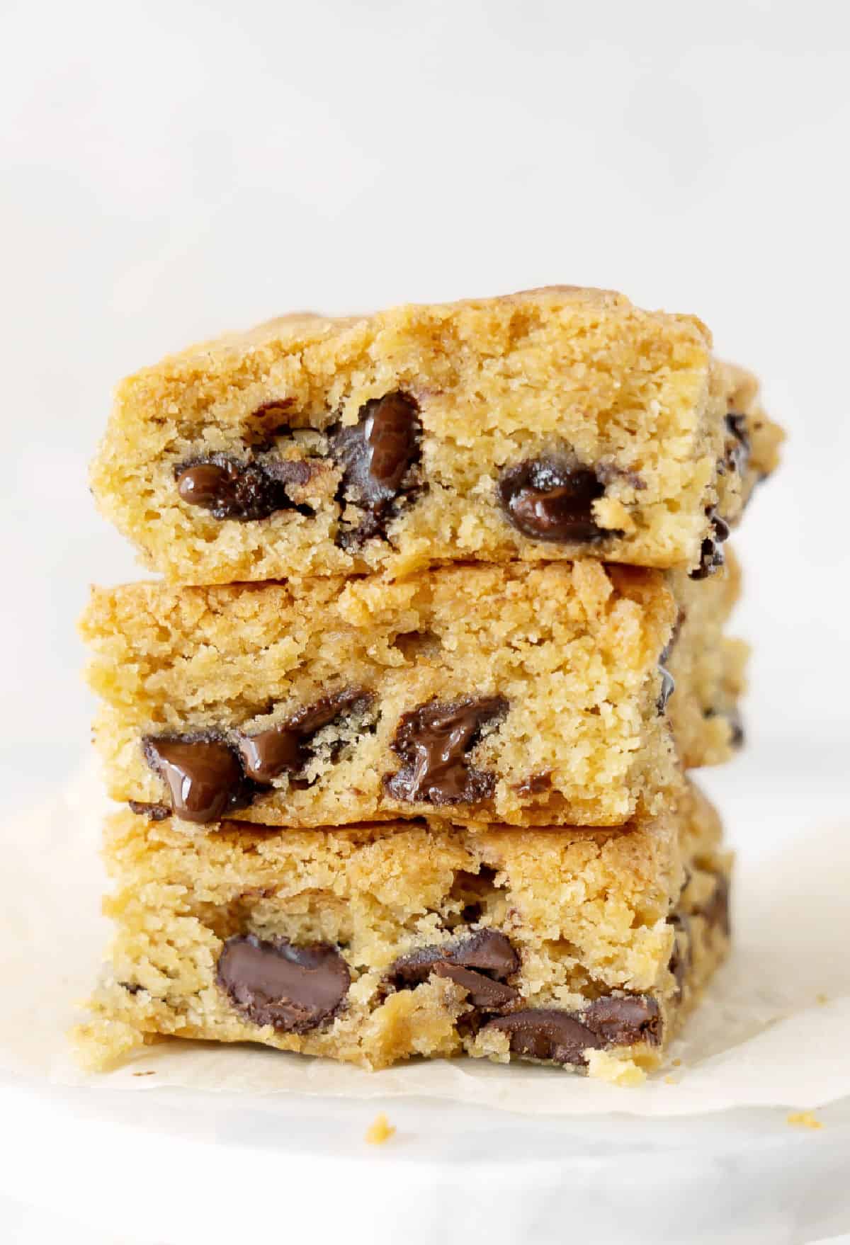 Close up stack of three chocolate chip blondies on a marble plate. Whitish background.