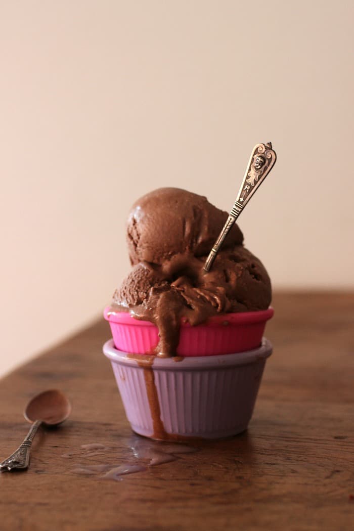 Wooden tables with purple and pink ramekins stacked with scoops of chocolate ice cream and spoon. 