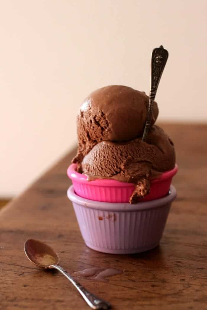 Scoops of chocolate ice cream on stack of purple and pink ramekins on a wooden table.