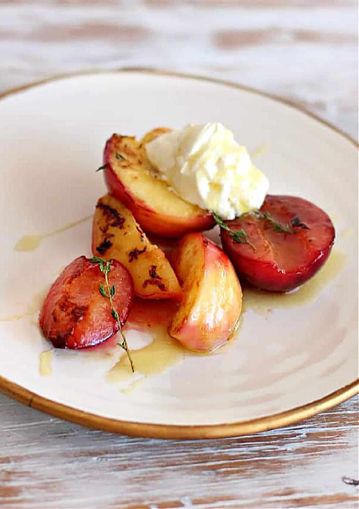 Halved peaches and plums on a white and gold plate with cream.