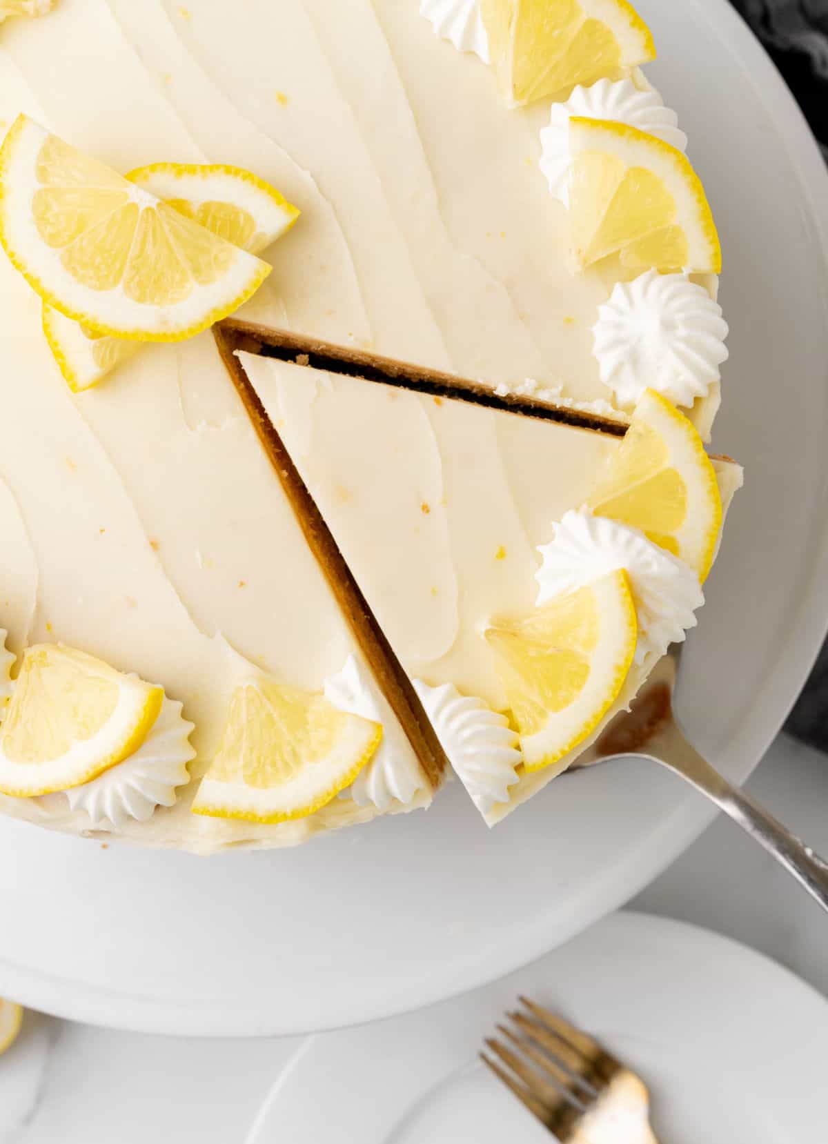 Top view of frosted lemon cake on a white cake stand. Cut slice being lifted. 