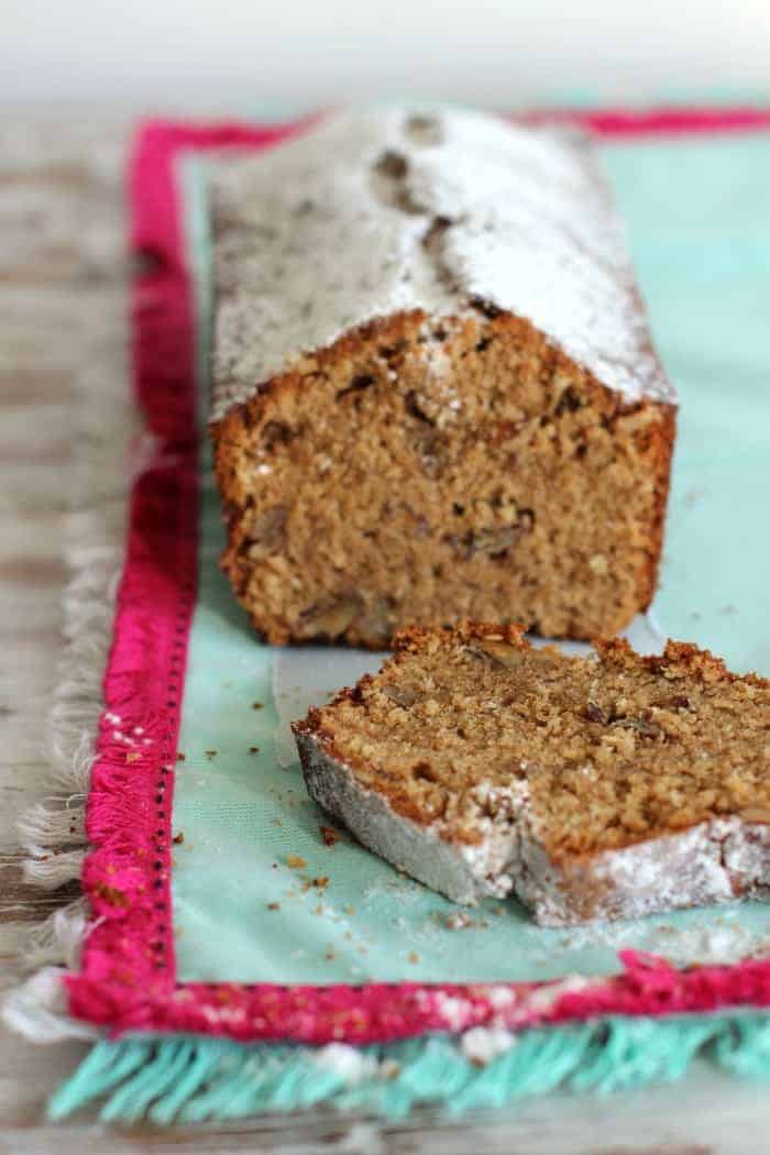 Slice and half loaf of coconut pecan cake on a minty green and bright pink kitchen towel. 