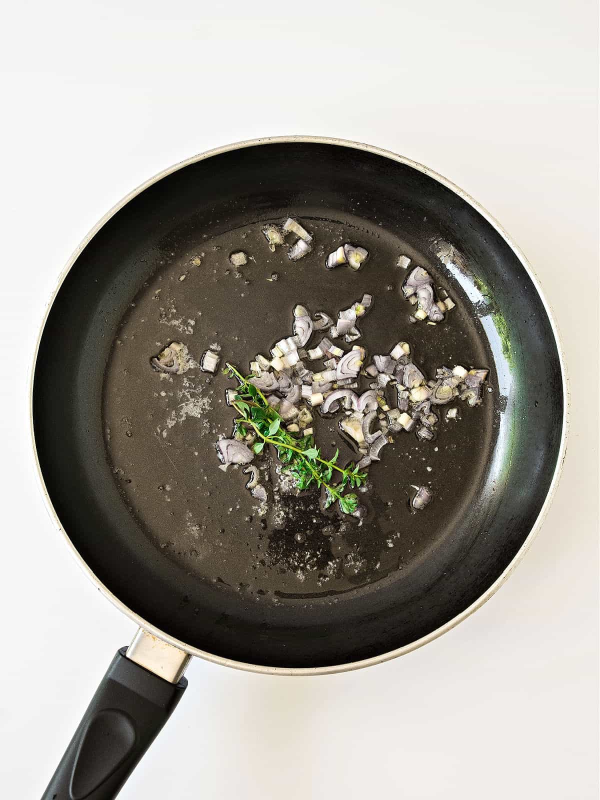 Shallots and thyme cooked in a black skillet. White surface.