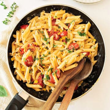Skillet with herbs, corn, tomato short pasta. White background.