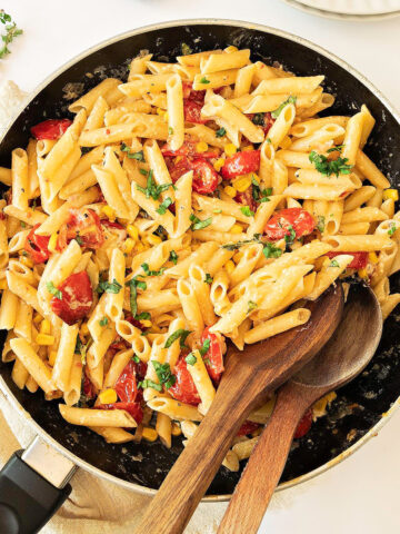 Skillet with herbs, corn, tomato short pasta. White background.