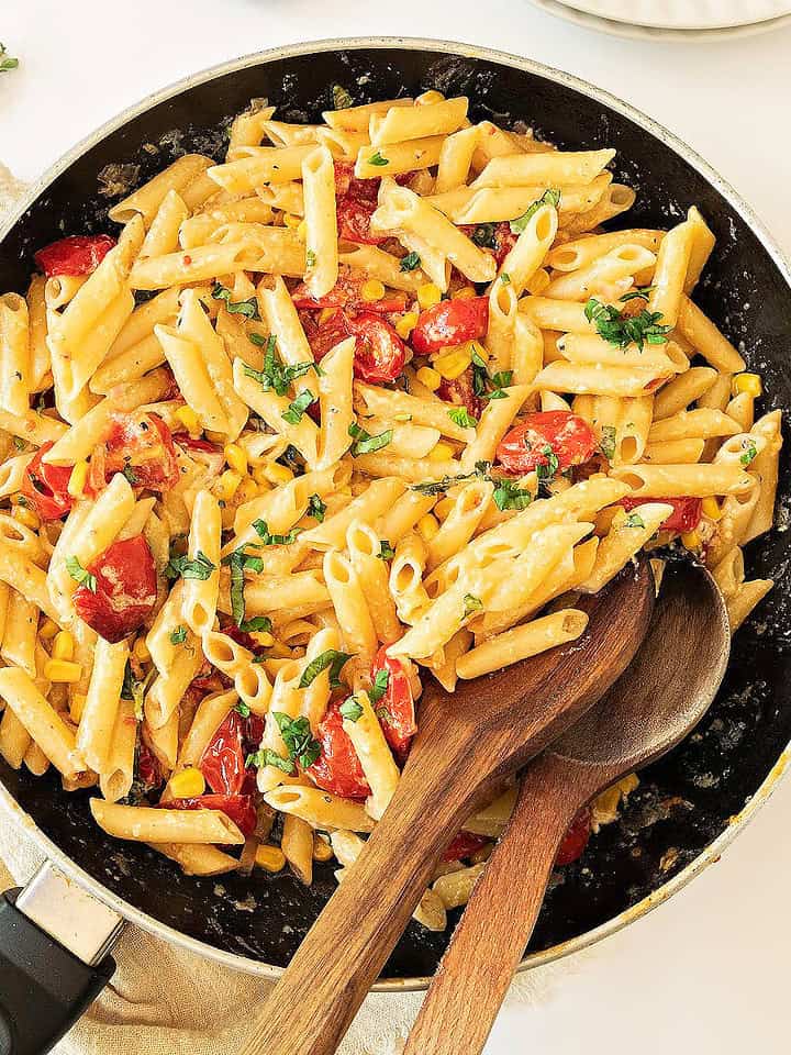 Skillet with herbs, corn, tomato short pasta. White background.