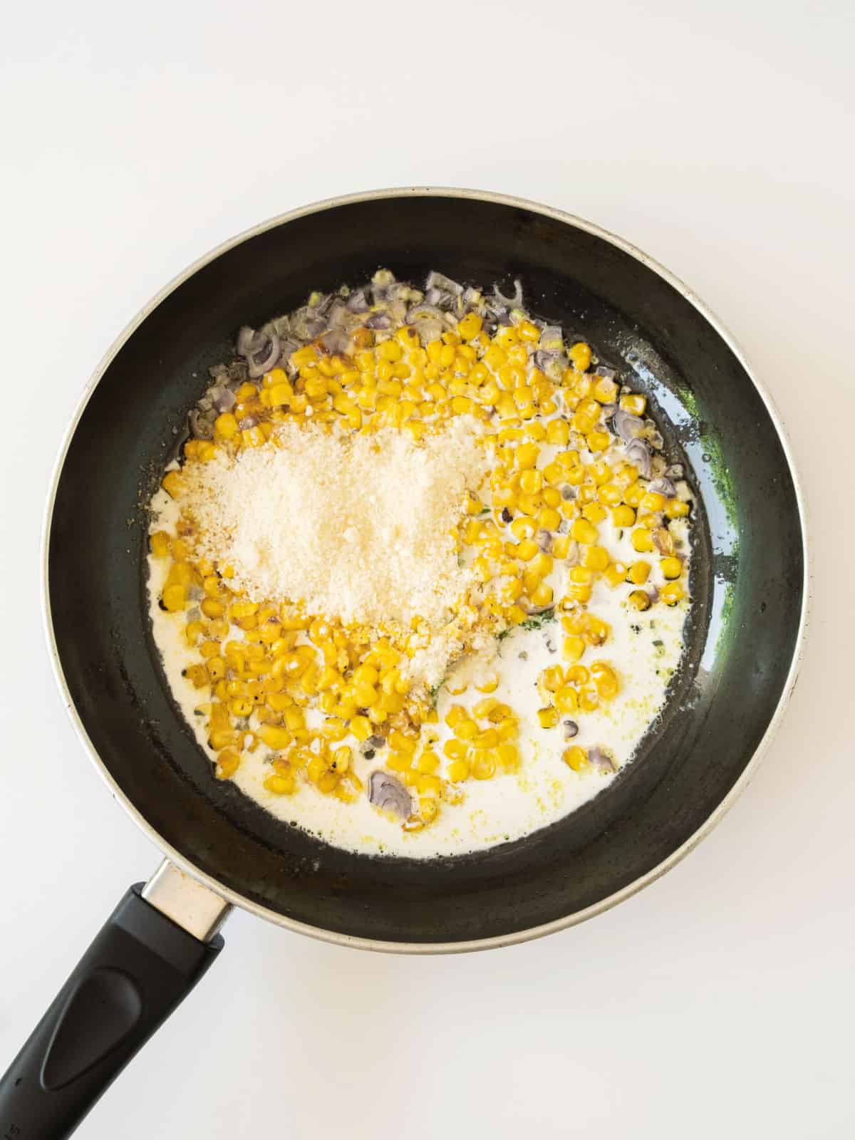 Cream, cheese and corn in a black skillet. Whitish surface.