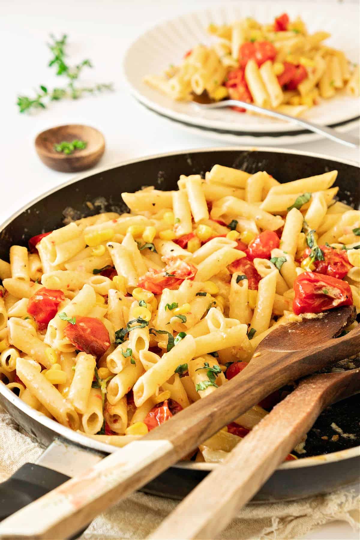 Black skillet and white plate with corn, tomato pasta. Wooden spoons.