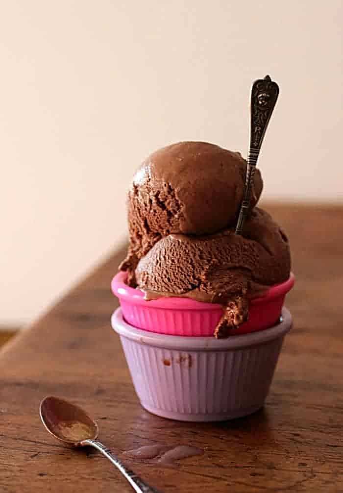 Purple and pink bowls with scoops of chocolate ice cream on a wooden board.